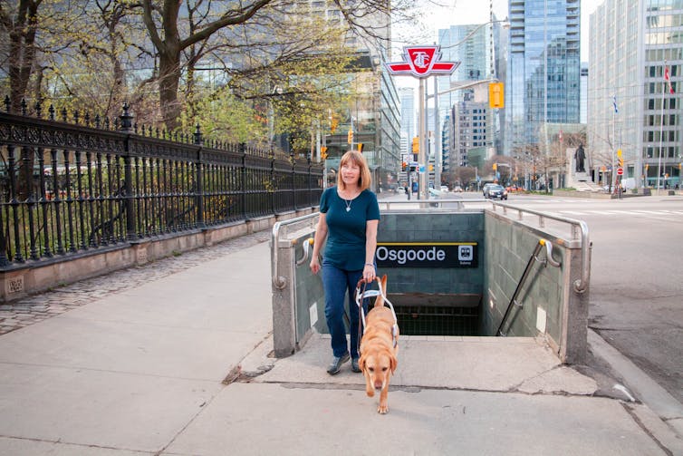 A woman walks near a subway station entrance with her service dog.