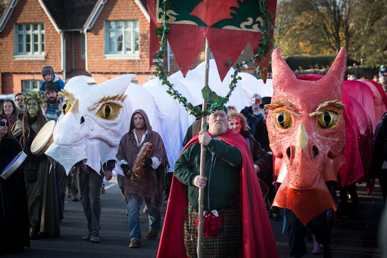 Man marches holding a flag with large fake dragons and costumed people behind him in procession.