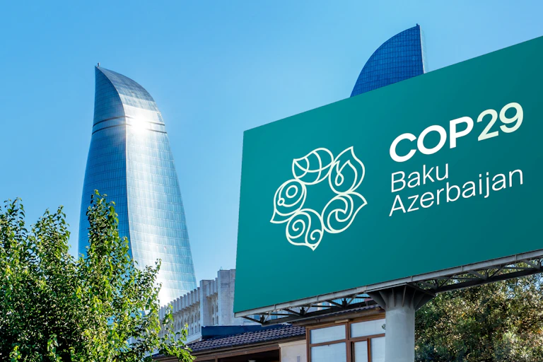 big green sign says COP29 Baku, Azerbaijan, outside, green trees, big silver skyscraper and blue skies