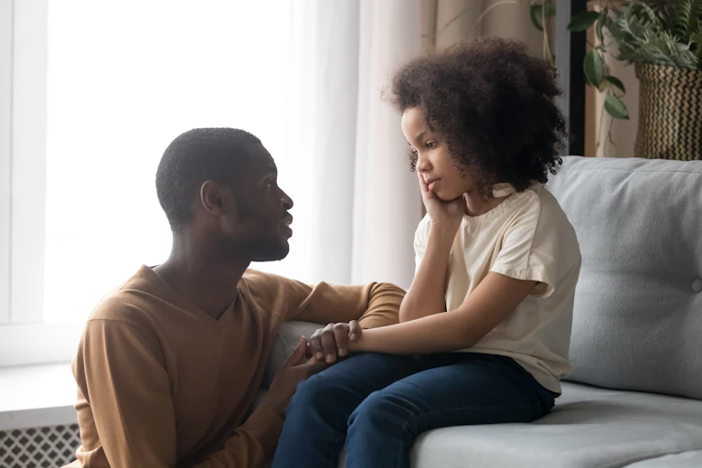 A father speaking to an upset child on a sofa