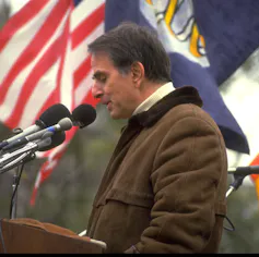 Carl Sagan standing behind a podium is delivering a speech.