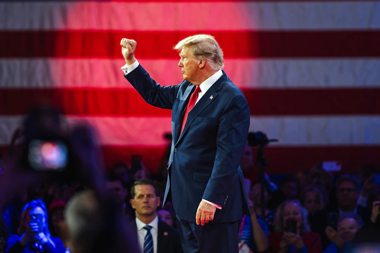 Donald Trump standing in front of a crowd with his fist raised.