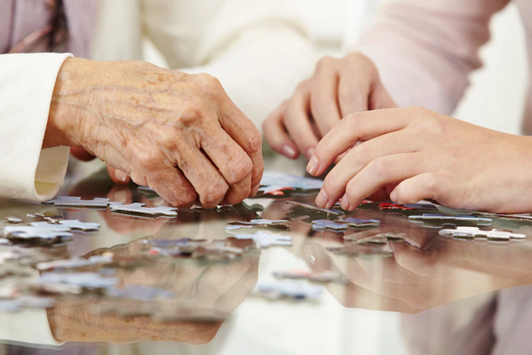 People's hands – young and old – doing a jigsaw puzzle.