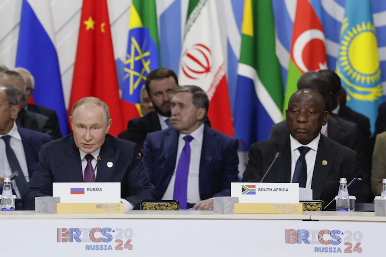 Men seated at a desk with national flags behind them