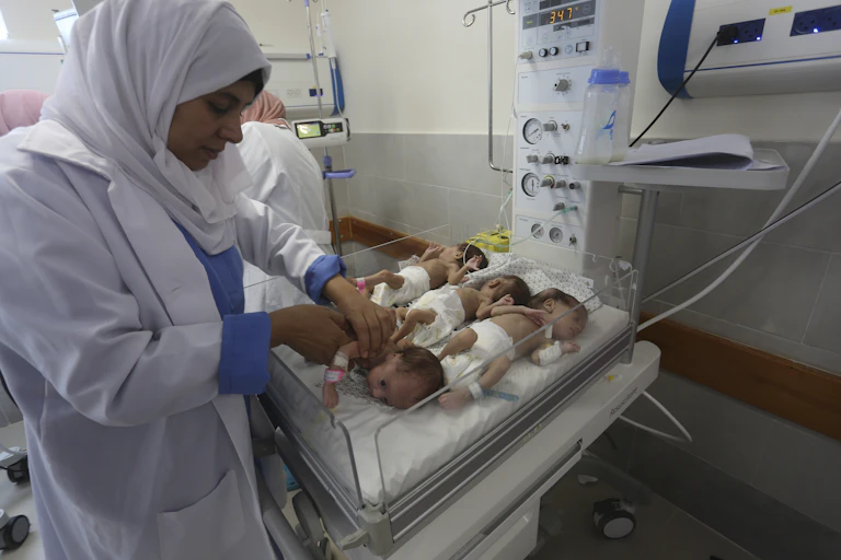 A woman in a white head scarf tends to small newborn babies.