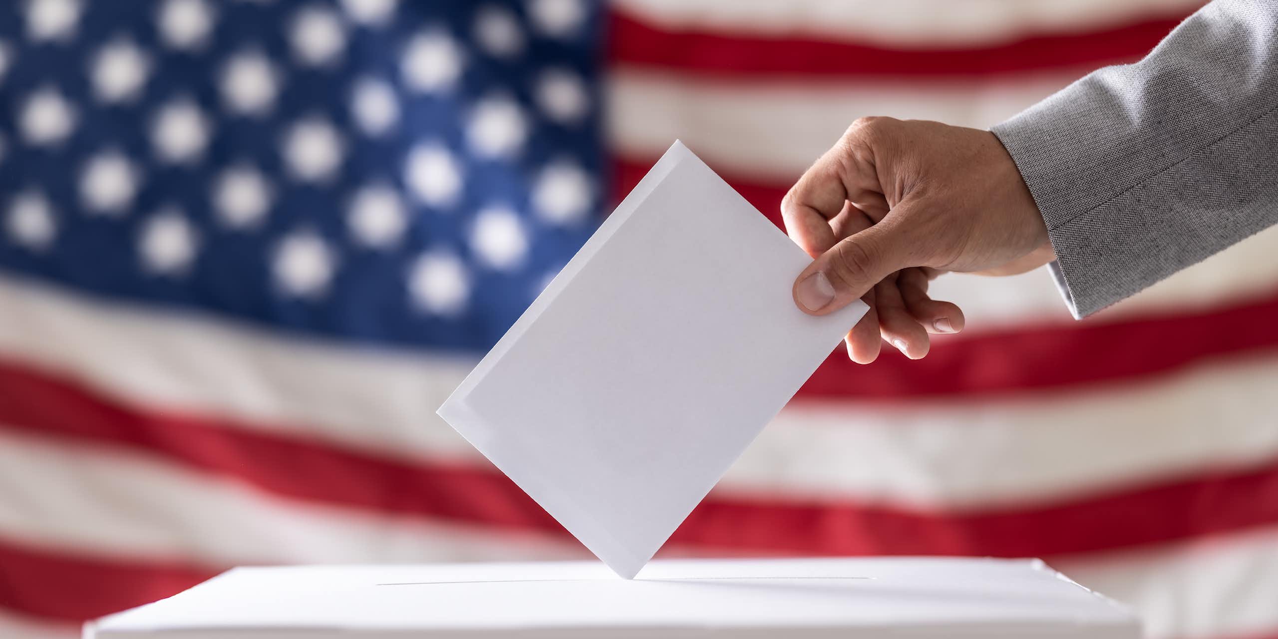 A person places a piece of paper in a box in front of a US flag.