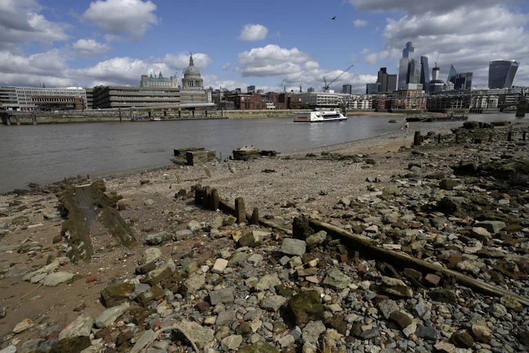 A river is seen at low tide as a boat sails past with buildings in the background.