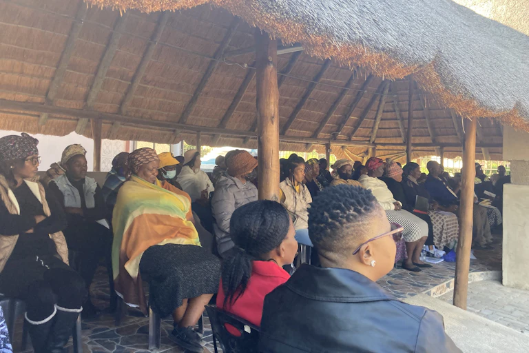A group of people sit under a thatched roof.