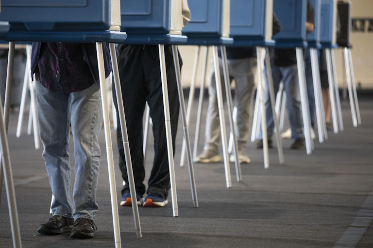 A row of people's legs are seen at blue booths.