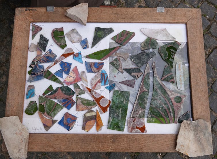 A tray set on the ground holds shards of brightly colored glass, including green, blue and red pieces.
