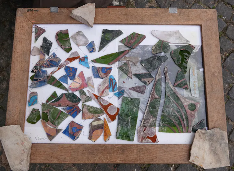 A tray set on the ground holds shards of brightly colored glass, including green, blue and red pieces.