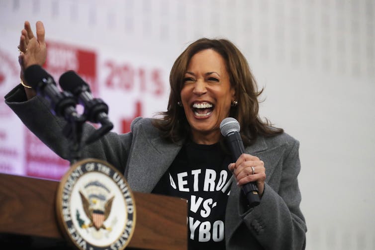 A broadly smiling woman raises her arm. She's wearing a black T-shirt with a suit jacket.