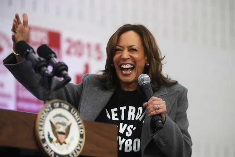 A broadly smiling woman raises her arm. She's wearing a black T-shirt with a suit jacket.