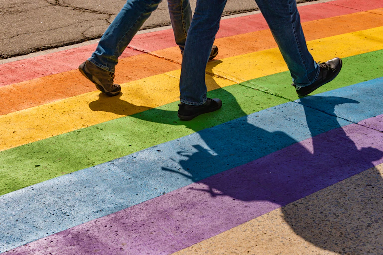 Lower half of men walking across rainbow crossing