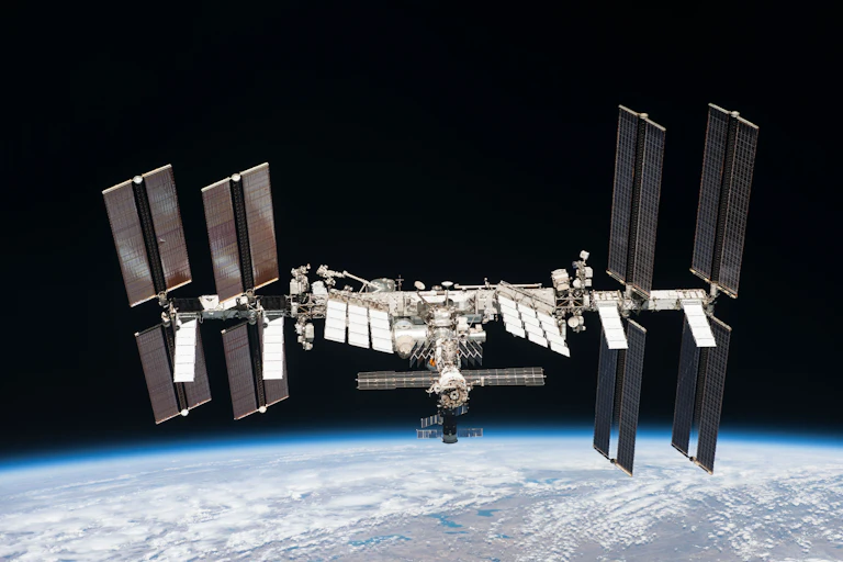 The International Space Station, which is a metal structure with solar panels coming off it, floating above Earth