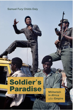 A book cover showing a man speaking into a microphone from the hood of a vehicle with an armed man standing next to him.