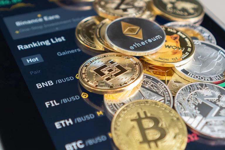 Gold bitcoin and silver ether coins against a Binance trading app screen.