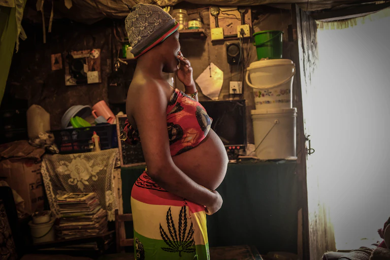 A heavily pregnant young woman, turned away from the camera, gently holds her belly with one hand
