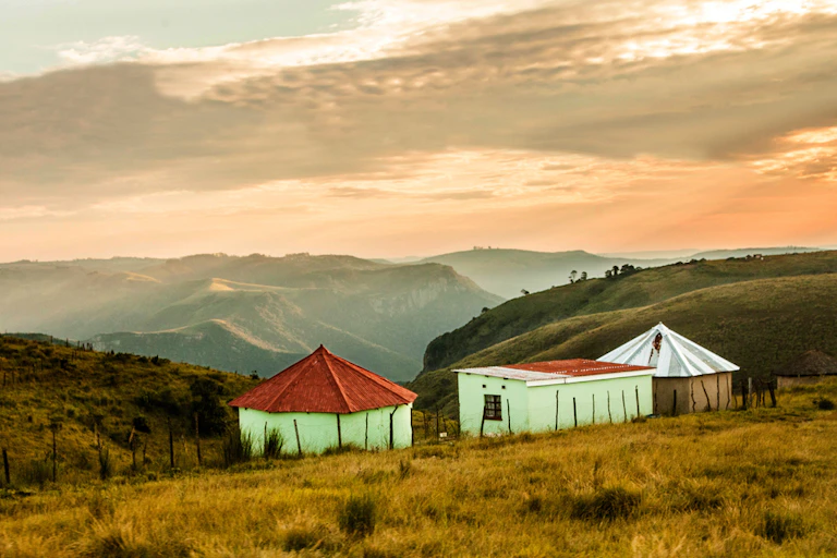 A landscape showing mountains and misty valleys, three huts in the foreground.