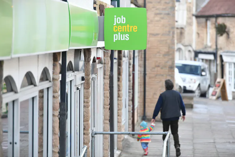 A man holding the hand of a young child walk into a job centre plus