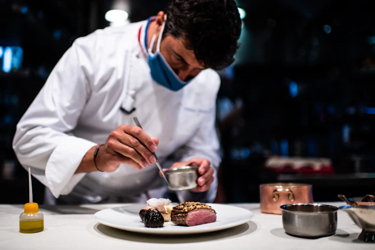 Le chef Yannick Franques dresse une assiette dans les cuisines de son restaurant, en portant un masque.