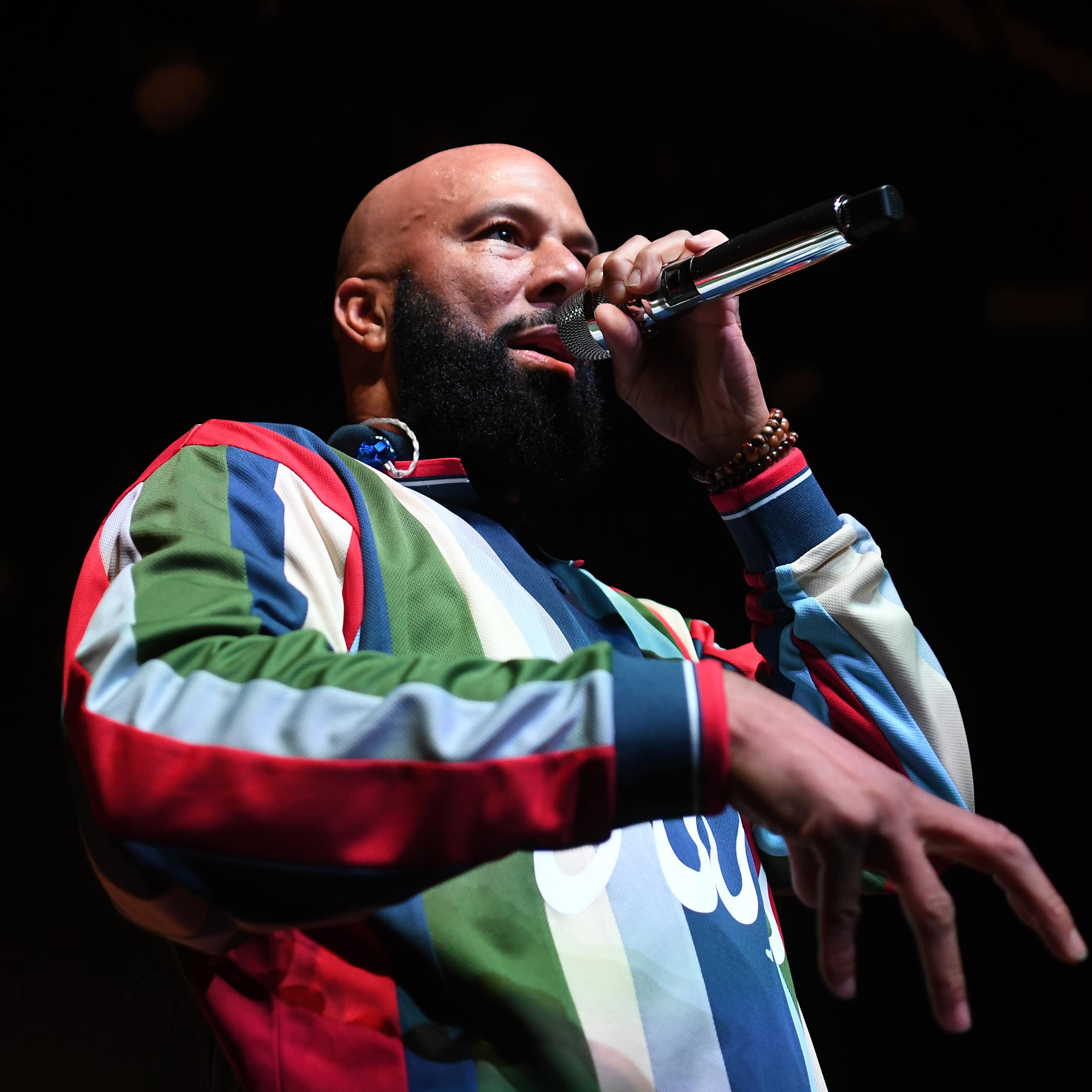 Bald bearded Black man wearing colorful shirt raps into a microphone.