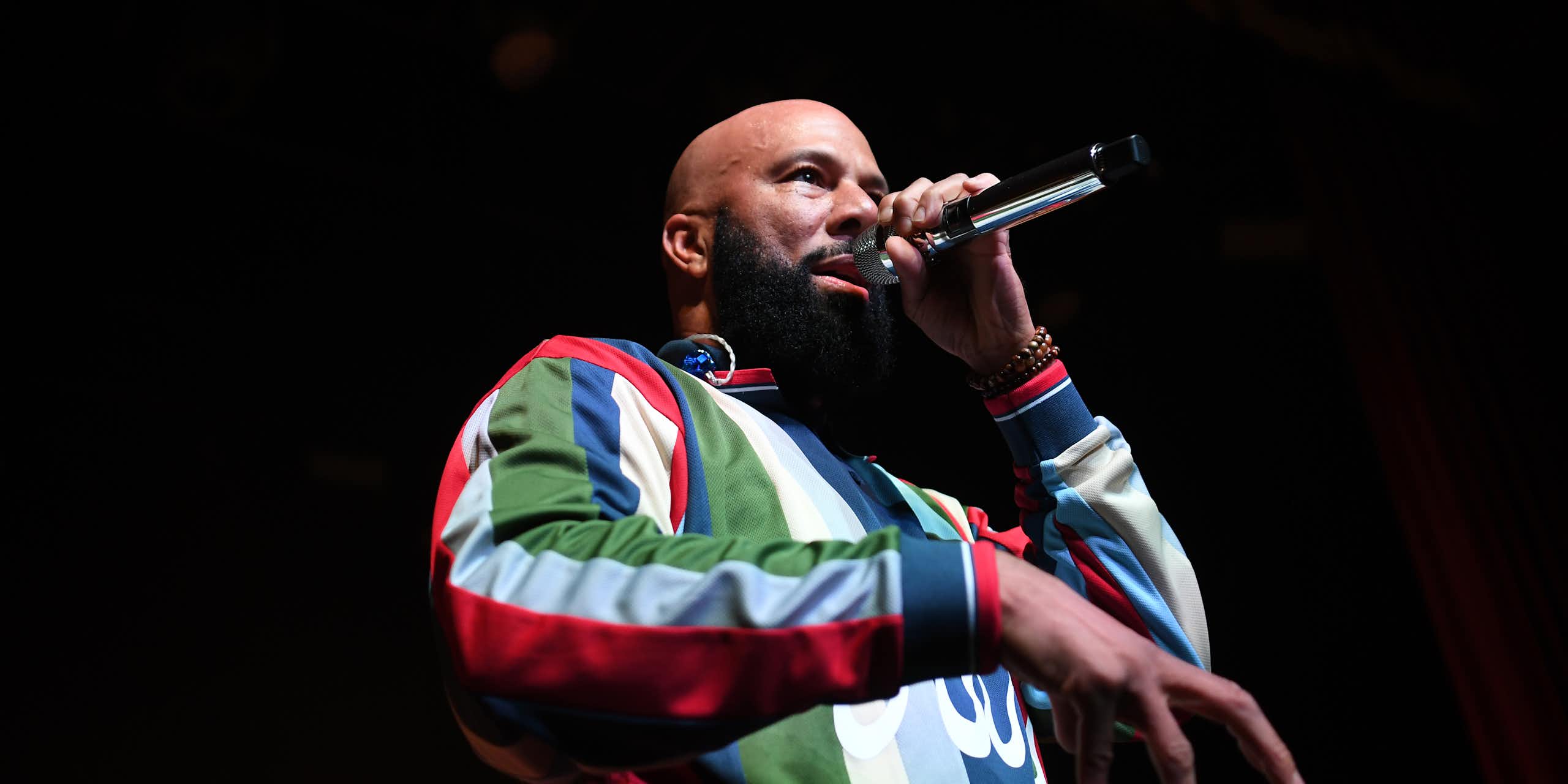 Bald bearded Black man wearing colorful shirt raps into a microphone.