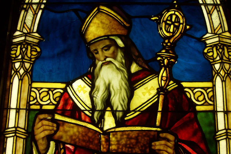 A richly colored stained-glass window of a man with a long white beard, red robe, and ornate staff.