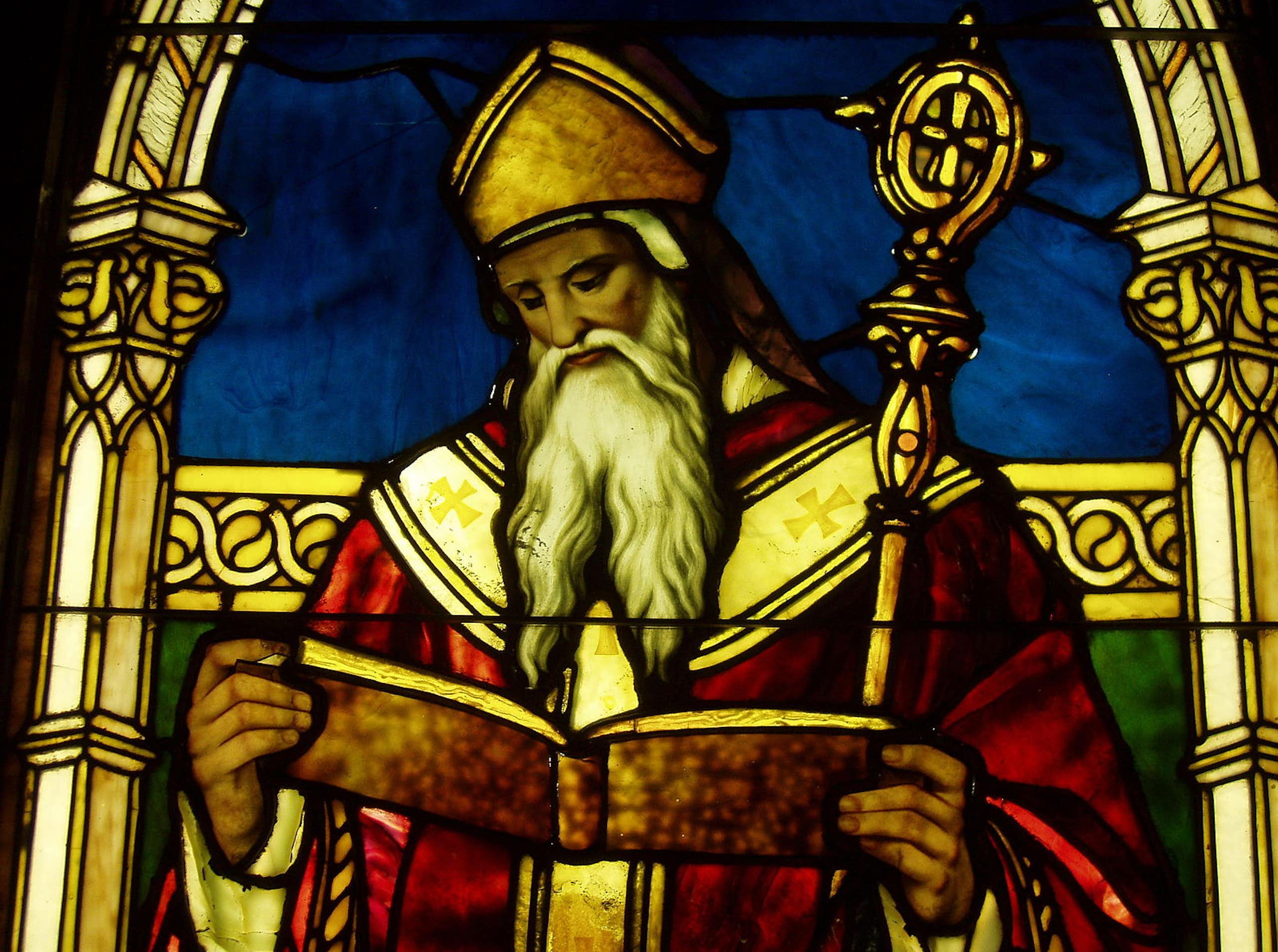 A richly colored stained-glass window of a man with a long white beard, red robe, and ornate staff.