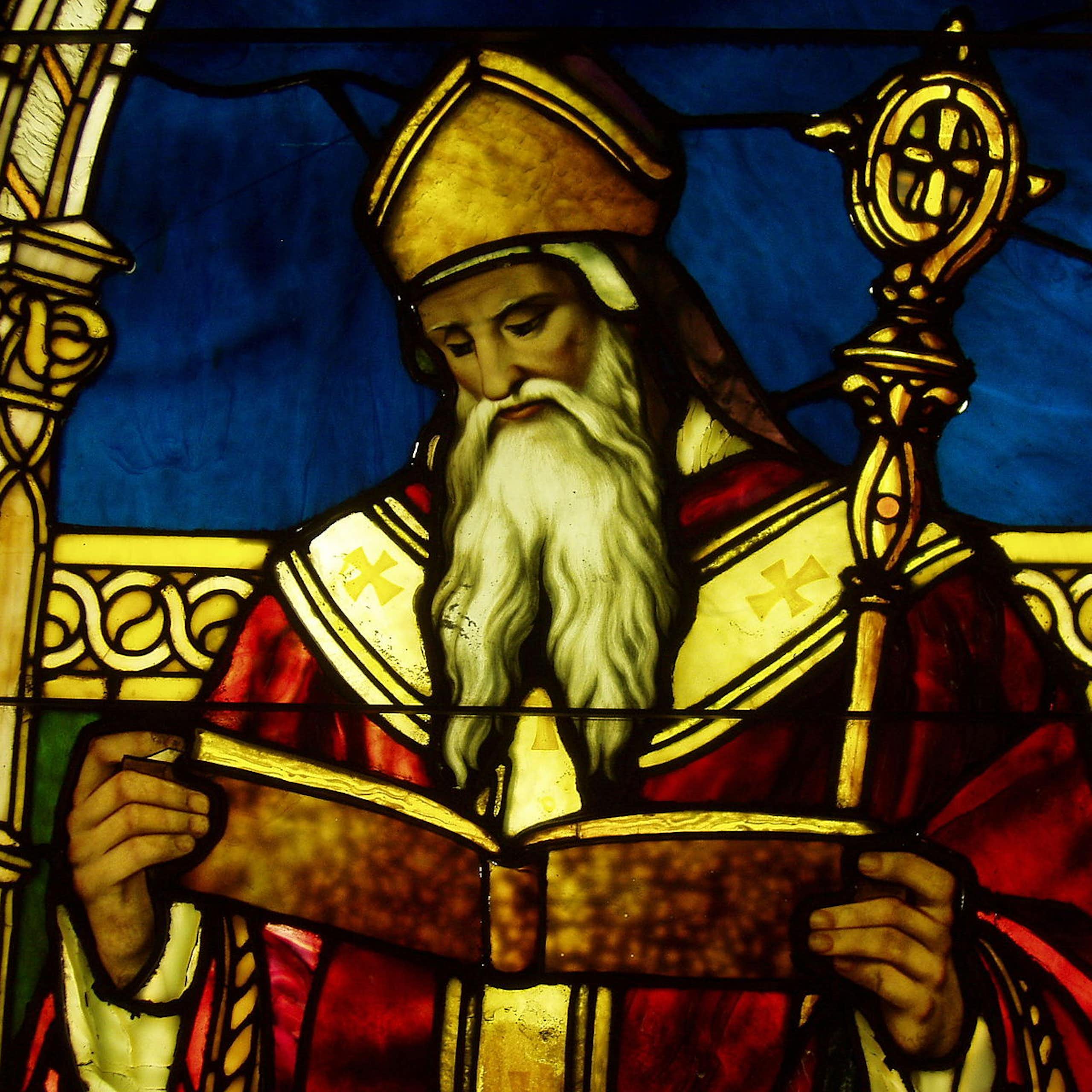 A richly colored stained-glass window of a man with a long white beard, red robe, and ornate staff.