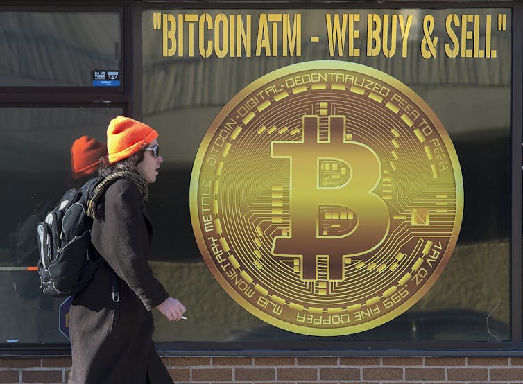 a woman in an orange hat walks past a poster of a large gold coin