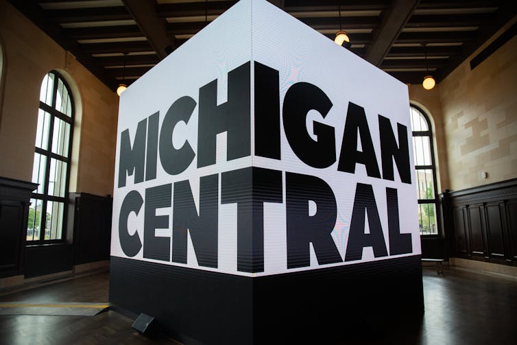 A huge screen inside a historic structure reads 'MICHIGAN CENTRAL'