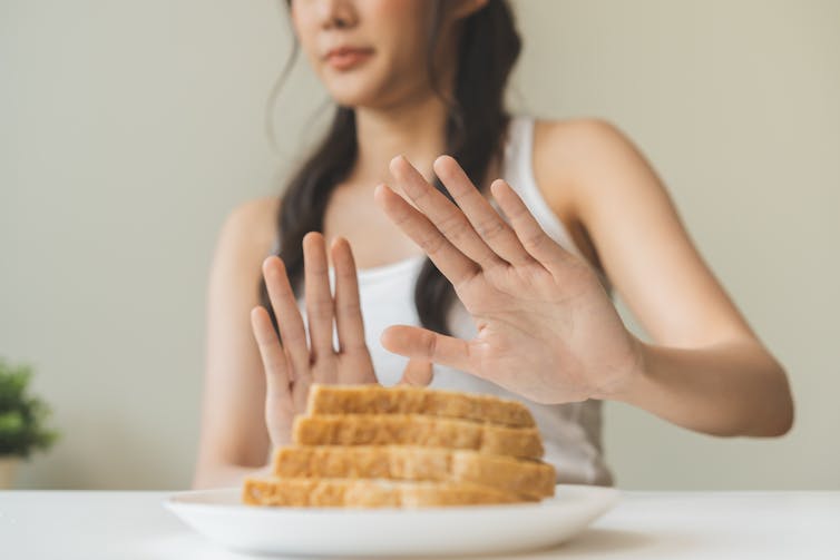 A woman cropped out of frame holding her hands up to refuse a plate of bread