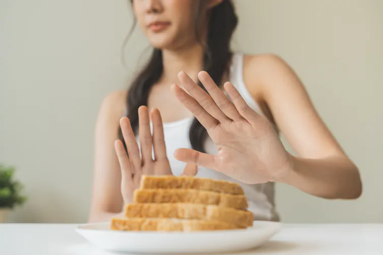 A woman cropped out of frame holding her hands up to refuse a plate of bread