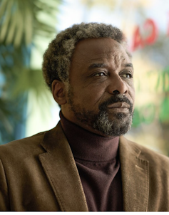 An older black man with greying hair and a beard staring off into the distance looking pensive.
