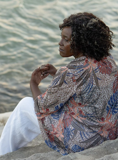 A beautiful older black woman sitting by the sea looking sad.
