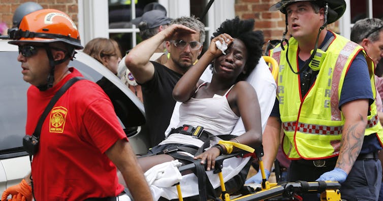 A Black woman weeps while being carried on a stretcher by paramedics.