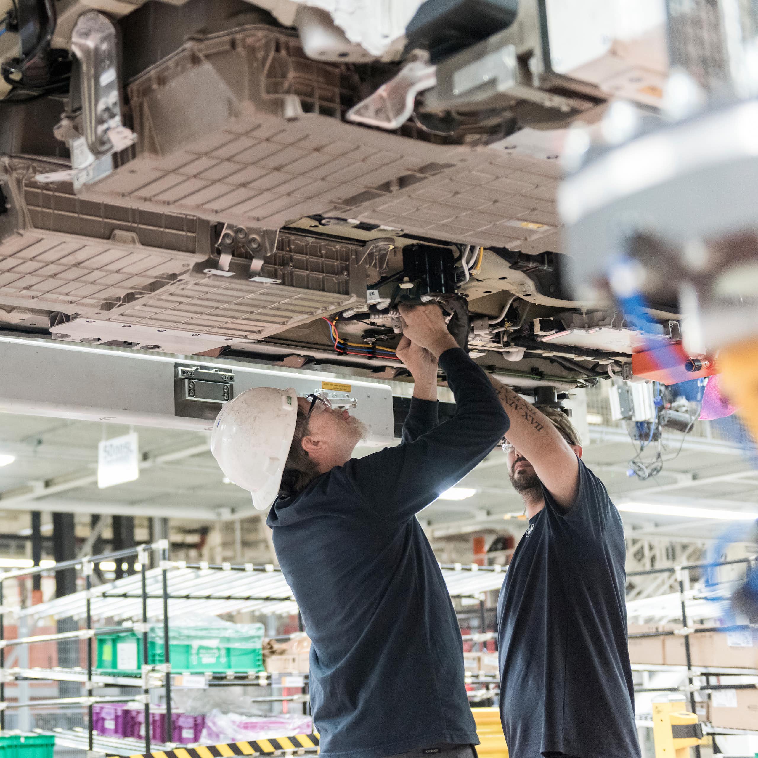Three workers install a battery under a vehicle being built.