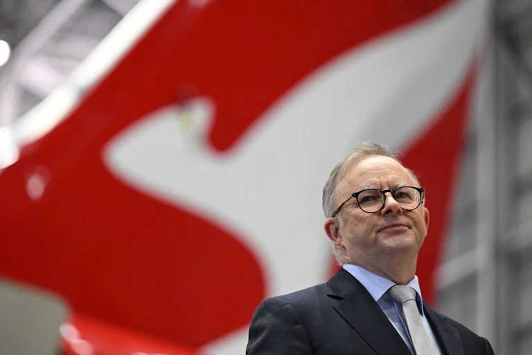 A man in a suit and glasses standing in front a a red tail of an airplane