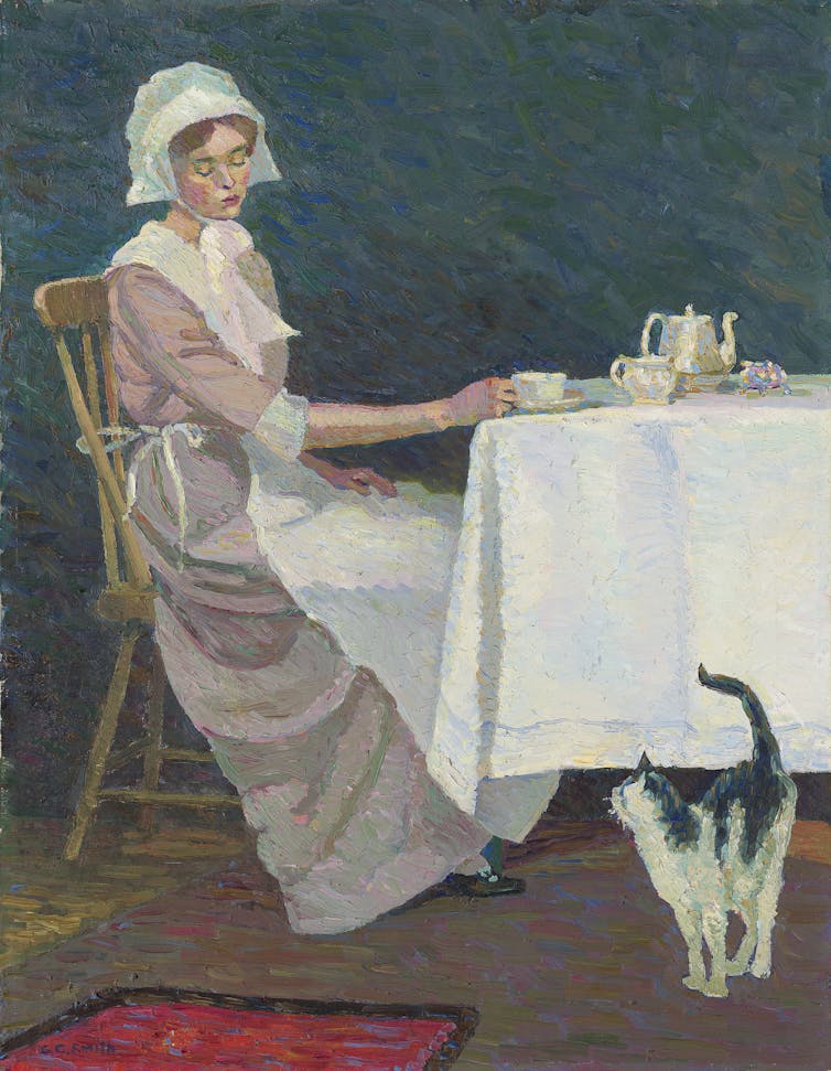 A woman sits at her table with a black and white cat.