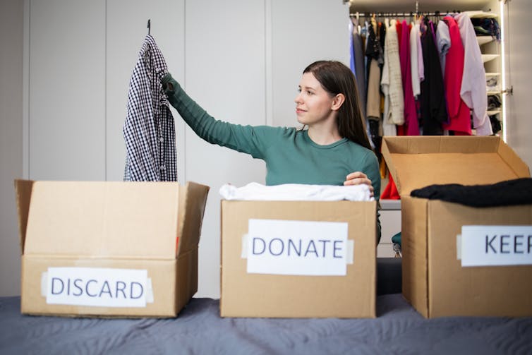 A woman sorts clothes into 3 boxes: discard, donate, keep.