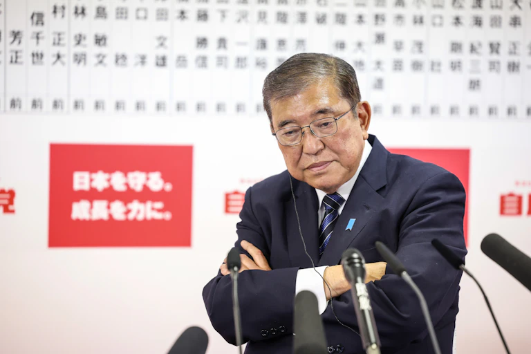 Shigeru Ishiba addressing the media with his arms crossed and a glum look on his face.