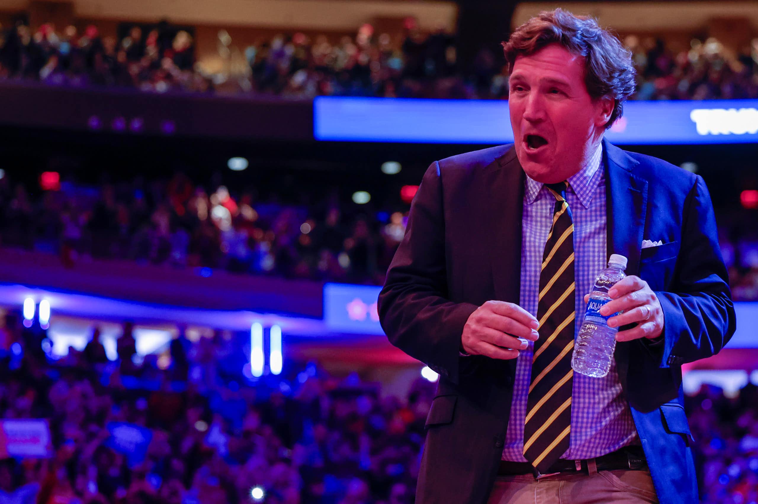 A preppy looking man with a bottle of water in his hand, laughing.