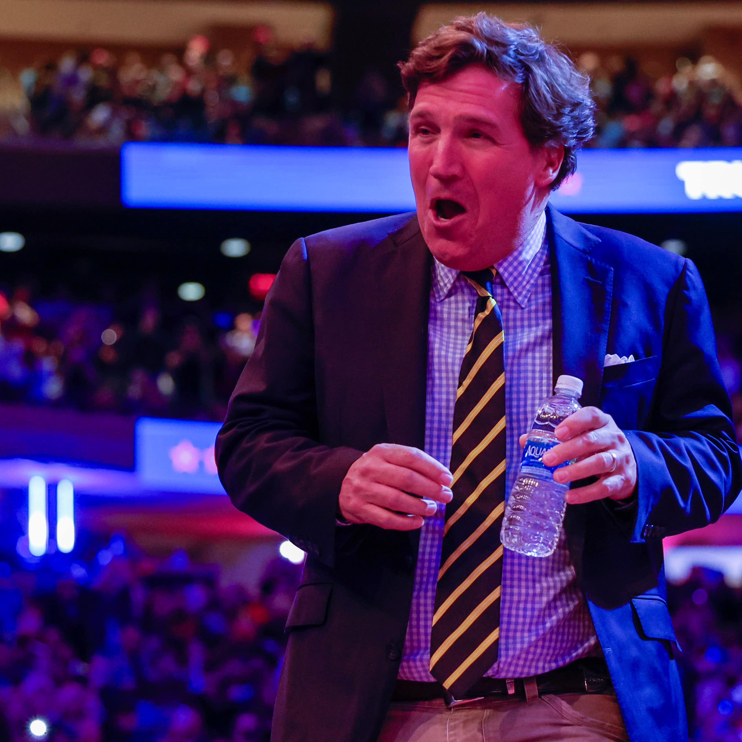 A preppy looking man with a bottle of water in his hand, laughing.