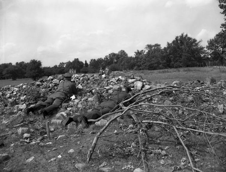 Men in uniform hide behind a pile of rubble in a field