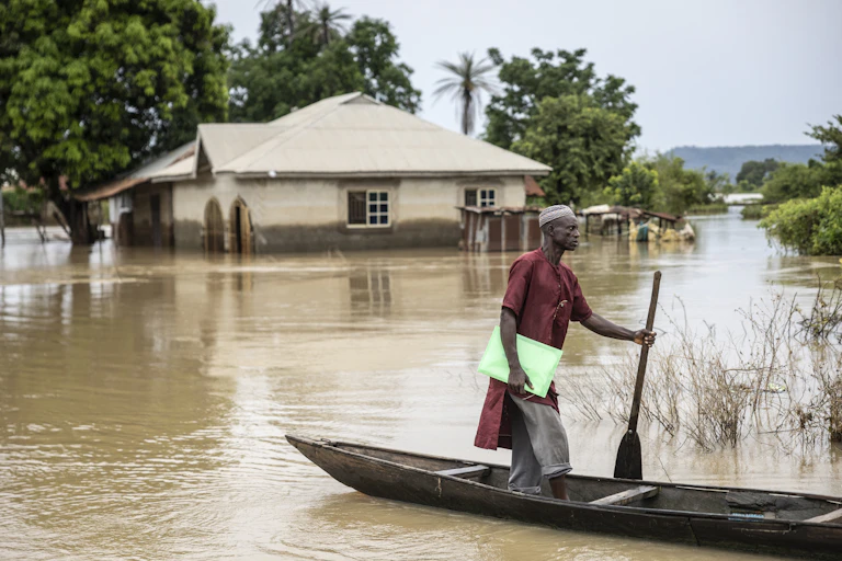 A man standing on a canoe surrounded by flood waters