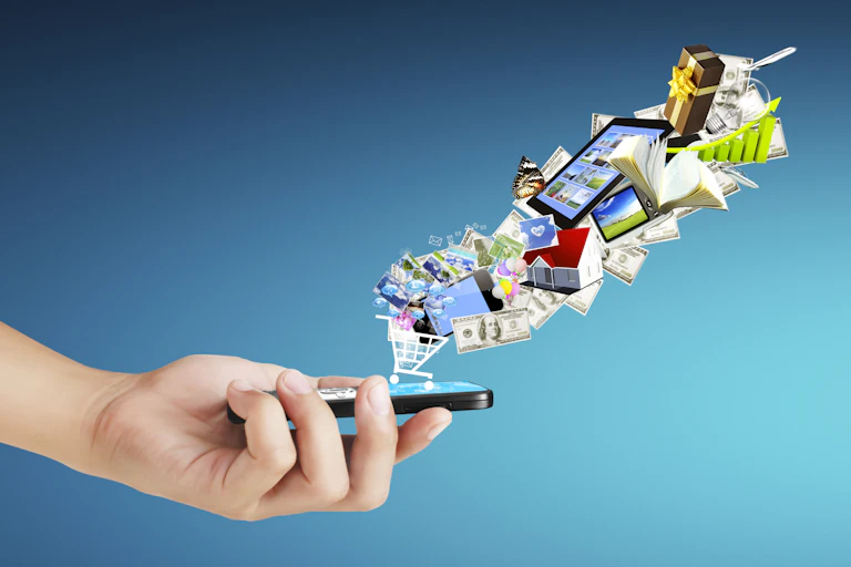 Illustration of hand holding smartphone with graphics of $100 bills and grocery carts and houses and books floating out of it.
