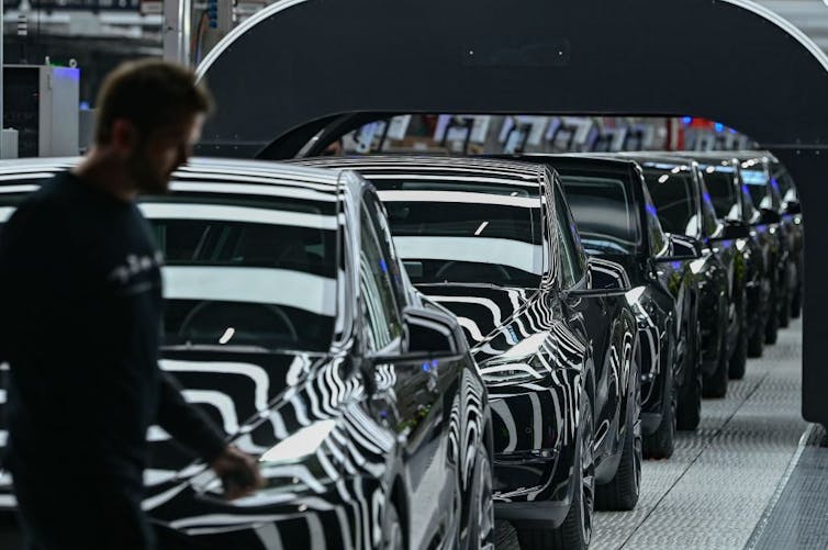 A succesion of sleek black cars on an assembly line.