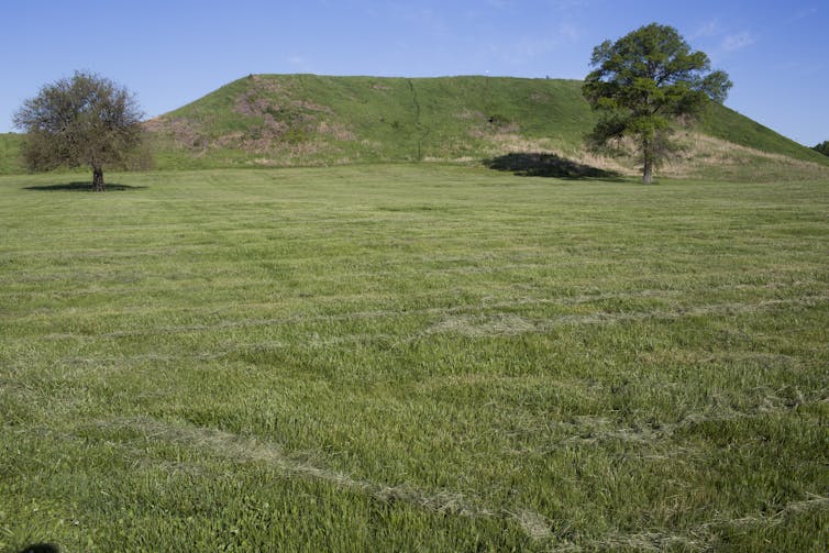 A flat grassy meadow with a large mound rising up in the background.