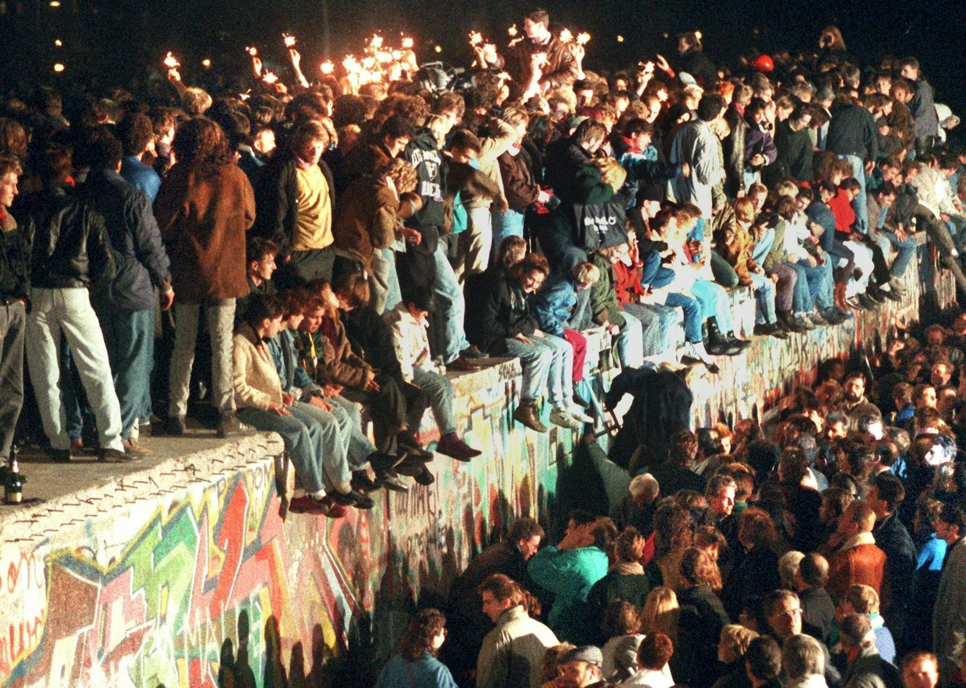 A historical photo of people standing and sitting on the Berlin wall as it is about to be torn down.